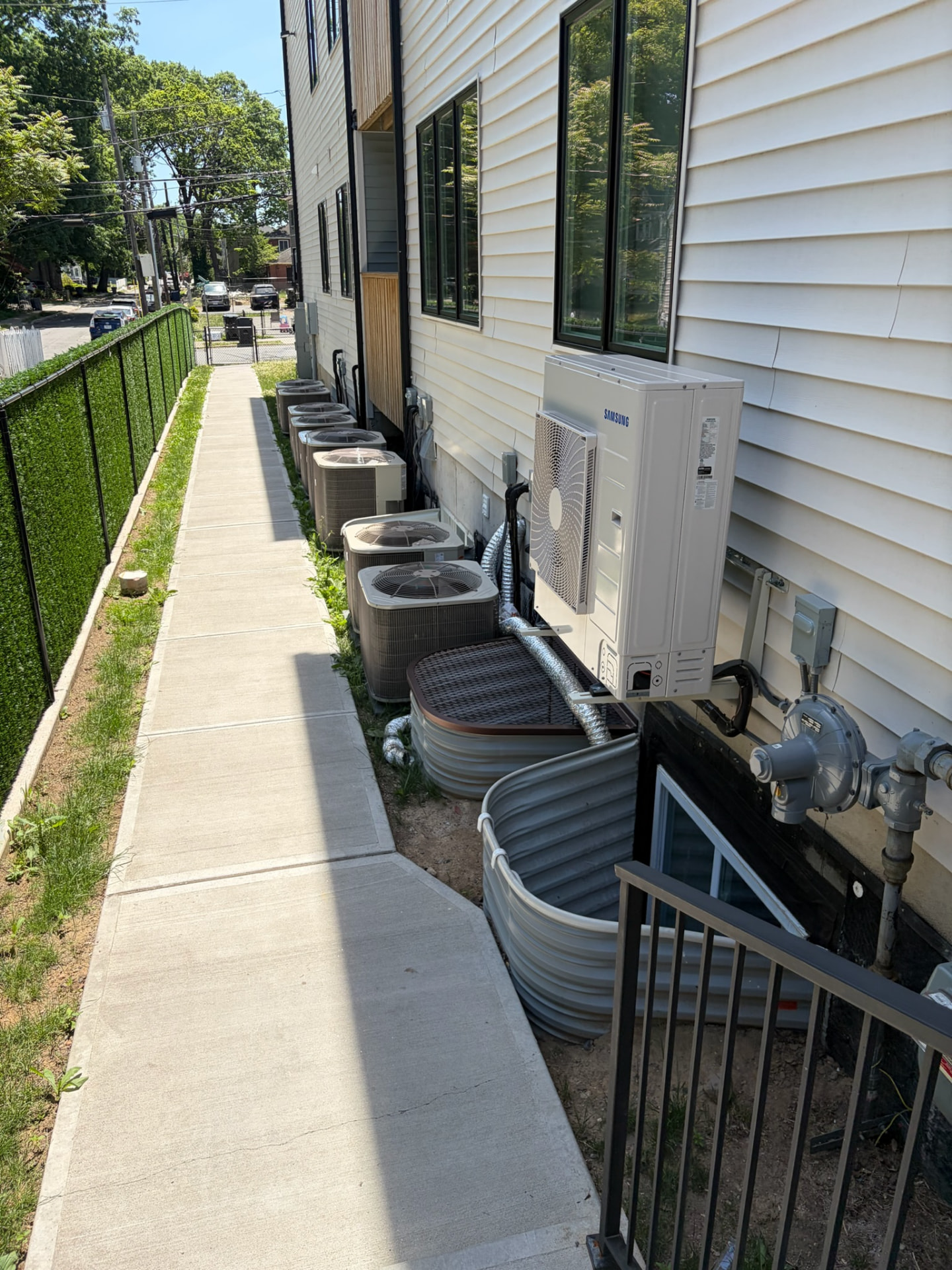 Row of outdoor heating and cooling units along the side of a building, with one unit mounted to the wall.